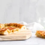 Close-up of artisan pizza dough with a bubbly, blistered crust and golden edges on a rustic wooden board.