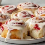 Fluffy strawberry lemon rolls with icing drizzled over golden brown spirals on a wire cooling rack.