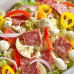 Italian sub salad deconstructed sandwich featuring chopped romaine lettuce, salami, pepperoni, ham, provolone cheese, tomatoes, red onions, banana peppers, and creamy Italian dressing in large white bowl.