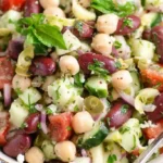 Mediterranean bean salad featuring chickpeas, kidney beans, white cannellini beans, cherry tomatoes, cucumber, bell peppers, kalamata olives, feta cheese, and fresh herbs with lemon vinaigrette in large white bowl.