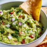 Guac cart style guacamole chunky and vibrant in a rustic stone molcajete bowl surrounded by tortilla chips fresh lime wedges and Tajín seasoning