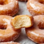 Homemade Glazed Donuts soft, golden yeast-raised donuts stacked on a cooling rack and coated with a glossy vanilla glaze, with a light drizzle pooling below